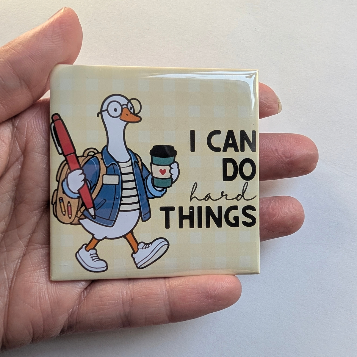 Hand holding the yellow I Can Do Hard Things goose fridge magnet against a white background to show its 2.5 inch size