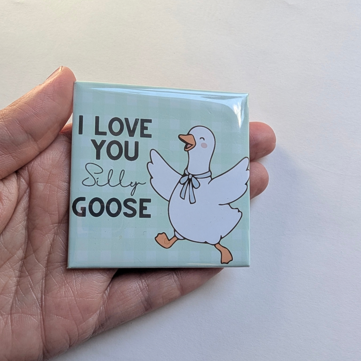Hand holding the mint green I Love You Silly Goose fridge magnet against a white background to show its 2.5 inch size