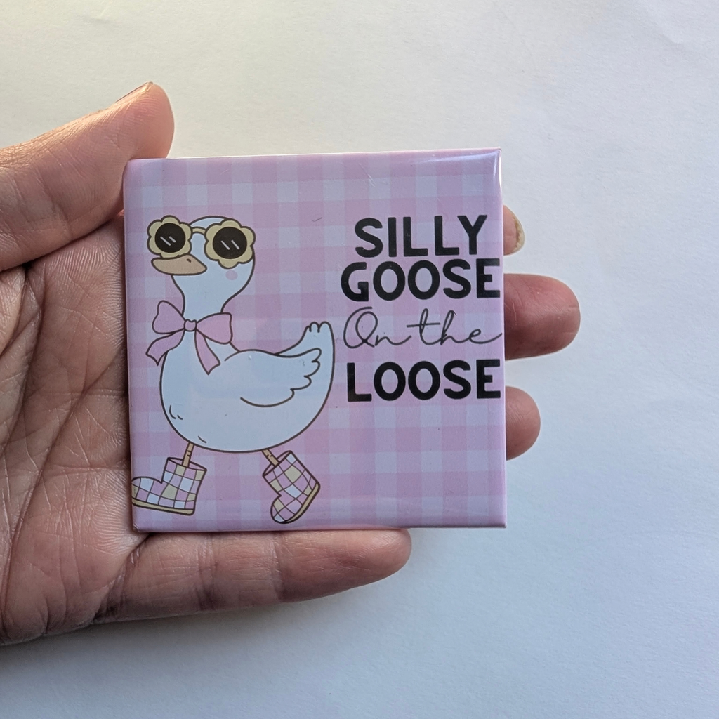 Hand holding the pink Silly Goose On the Loose fridge magnet against a white background to show its 2.5 inch size