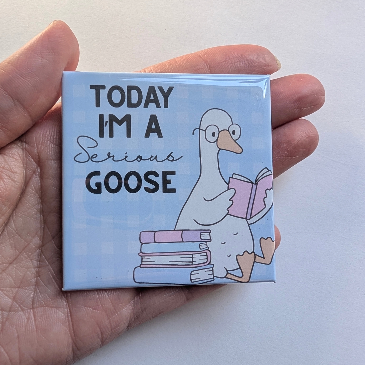 Hand holding the blue Today I'm a Serious Goose fridge magnet against a white background to show its 2.5 inch size